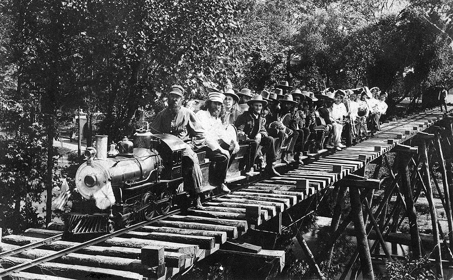 Since a deep valley cut through the middle of the property, it was necessary to build two wood trestle bridges at the park's east and west ends. For passengers the effect was of the train flying through the air above the park. The passengers of this early view are the colony's musicians.