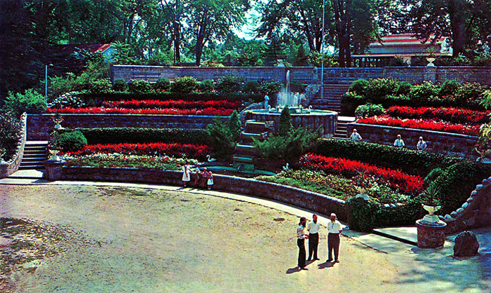This Fountain was constructed in the Mid 50's by the Bank Construction people.  It had colored lights on the water spray.  In the summer evenings it was run daily.  Chic Bell was its founder.  The fountain superseded the Auditorium which had been torn down.  In this picture the three men on the right are William Robertson, printer, Alec Robertson, forester and road maintainer, & George Wackym, business man.  The children in front of the fountain are Margret, Alec Jr., Bruce and Irene.  The three men left to right at the wall are Percy Minchington, souvenir stand operator, Dominic, florist, and Charlie Jeff, printer, garden supervisor.
