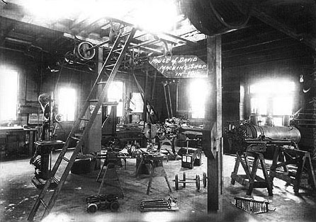 This view of a colony machine shop shows a disassembled miniature locomotive. The boiler on saw horses to the right is from the original Cagney engine purchased in New York. Colony members constructed blueprints from this engine to build other locomotives. The other parts displayed include parts of this engine which were cannibalized in the winter of 1908-9 when construction began on four 4-4-0 American Standard type engines. This original engine, with a larger boiler and other reinforced parts became locomotive #5 on the M&B (Mary and Benjamin line).